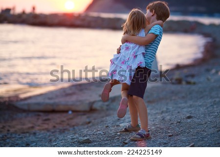 A young happy boy and his little cute sister walking on the sea shore on a warm summer evening. Friendship between siblings.