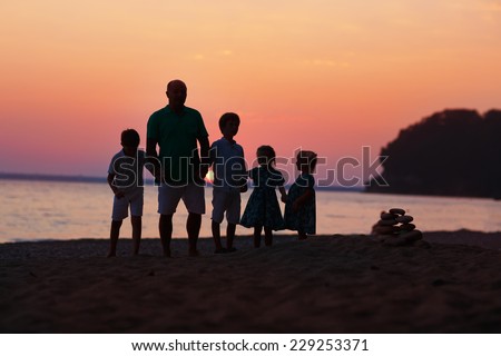 Silhouettes of a happy family: a strong healthy man and his grandchildren - little boys and girls standing on the sea shore and looking to the sunset on a warm summer evening