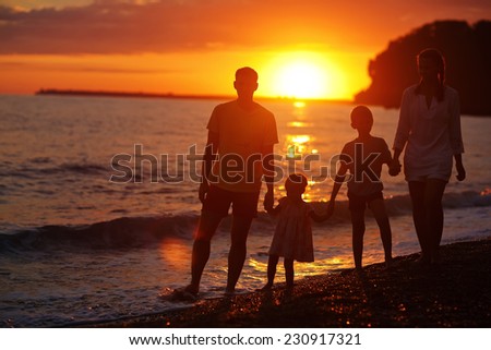 Silhouettes of a happy family: a strong healthy man, his young wife and their children - little boy and girl standing on the sea shore and looking to the sunset on a warm summer evening