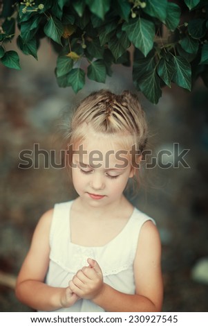 A close up portrait of a sweet smiling little girl in a white dress dreaming about something