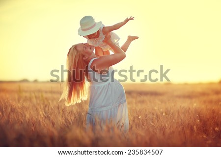 Happy family: a young beautiful pregnant woman with her little cute daughter walking in the wheat orange field on a sunny summer day. Parents and kids relationship. Nature in the country.