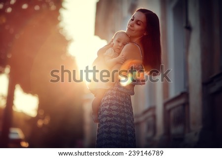 A young beautiful slim woman in a blue dress with her little cute baby walking around the old town on a sunny summer day.