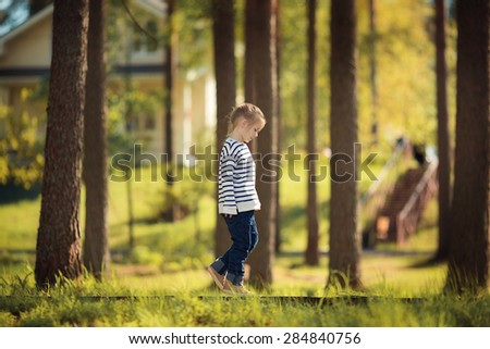 A pretty little girl in a striped sweater walking in the forest surrounding the cottage on a sunny spring day