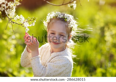 A lovely little girl with a diadem of white flowers standing under a blooming cherry tree on a sunny spring day. Kids and flowers close up.