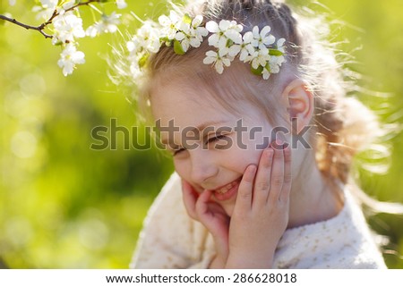 A lovely little girl with a diadem of white flowers standing under a blooming cherry tree on a sunny spring day. Kids and flowers close up.