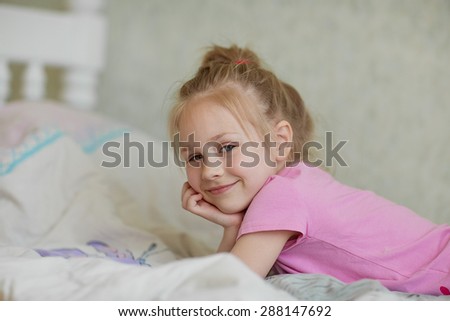 A close up portrait of a sweet smiling little girl in pink pajamas lying in bed in the morning
