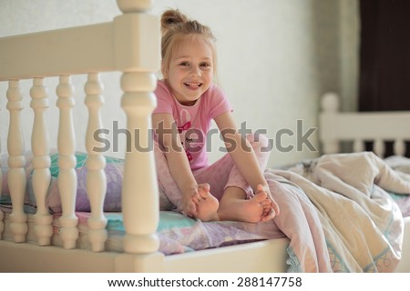 A little sweet smiling girl  in pink pajamas waking up and sitting on the bed in the morning