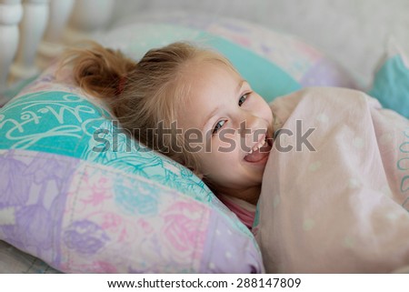 A close up portrait of a sweet smiling little girl waking up and lying in bed in the morning