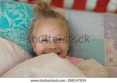 A close up portrait of a sweet smiling little girl waking up and lying in bed in the morning