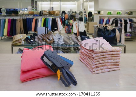 Pricing, store, desk.. Price gun on folded clothes of counter in retail shop interior.