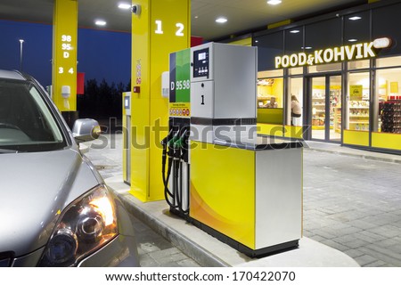 Car in gas station. Fuel, petrol dispenser, pump, handles and pillars. Fueling. Estonia. Lighted window of convenience store and coffe shop.