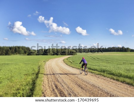 Woman cyclist. Cycling on unpaved winding road in Estonia. Agricultural landscape, field.