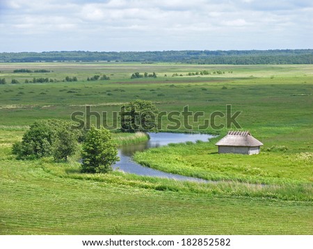 Rural landscape with wooden log cabin by river