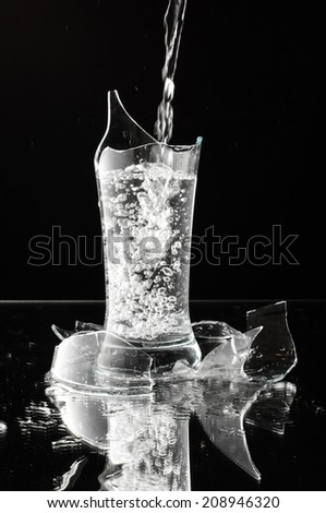 Spout of water in the fragments of glass isolated on the black background