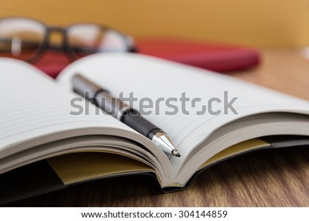 book with pen, mobile and keyboard on desk