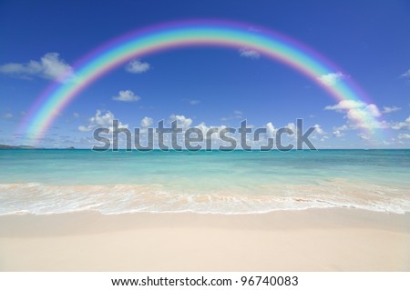 Colourful rainbow over a blue ocean with sandy beach in the foreground