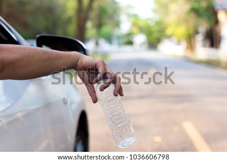 man\'s hand throwing plastic bottle out of car window, close up