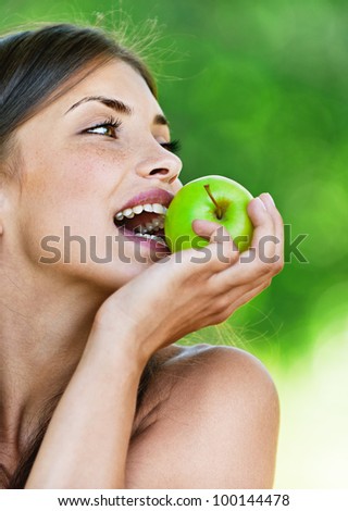 portrait young charming brunette woman biting green apple background summer park