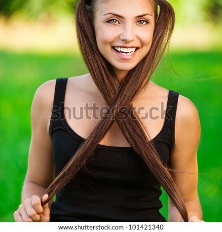 Portrait of an elegant, young, long-haired woman with two tails crossed them under the chin background summer green park