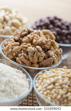 Shelled walnuts, cashews, sesame seeds, pine nuts in glass plates on bamboo table cloth.