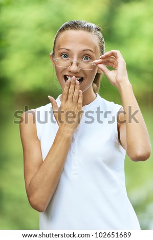 Beautiful young woman is surprised with his hand covering mouth, against green of summer park.