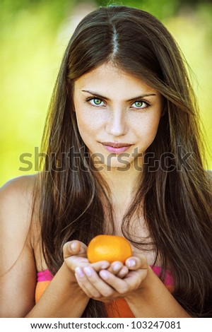 Portrait of young beautiful woman holding tangerine, on green background summer nature.