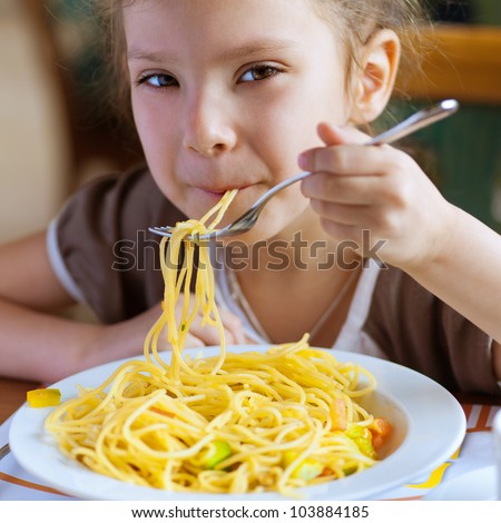 Small girl eating spaghetti with fork and smiles.
