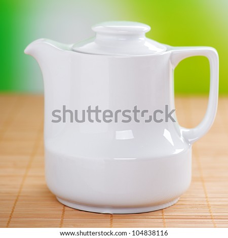 White small jug of milk costs on bamboo table cloth, on a background of green summer garden.