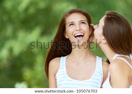 Girl tells her friend gossip, against green of summer park.