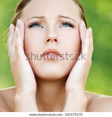 Young beautiful woman keeps hands for head and looks upwards at summer green park