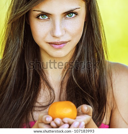 Portrait of young beautiful woman holding tangerine, on green background summer nature.