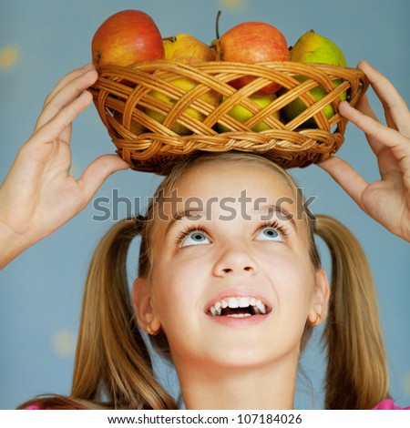 Beautiful blue-eyed laughing girl-teenager in pink dress keeps on his head basket of apples, on blue background.