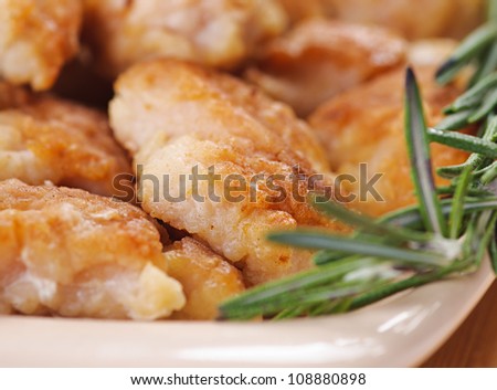 Fried chicken pieces in a plate on wooden table.