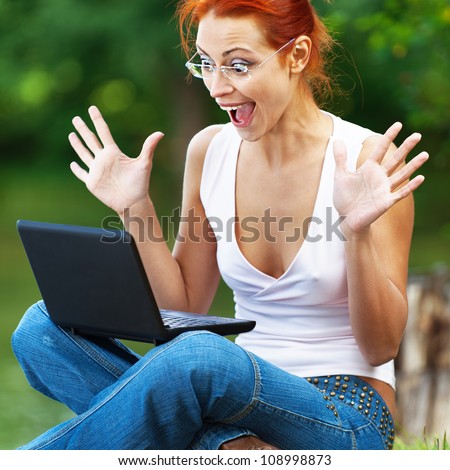 Carroty beautiful woman with joy and delight in watching laptop screen, on green park summer.