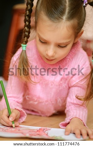 Preschooler in pink sweater draws a pencil on paper.