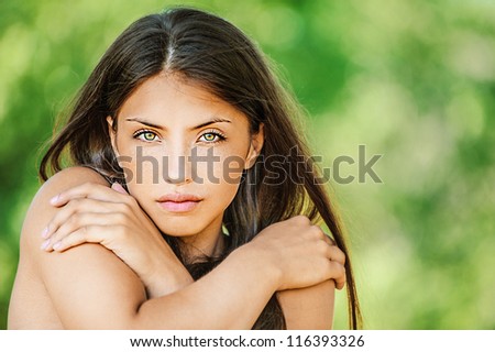 Portrait of young beautiful woman with bare shoulders crossed her arms, on green background summer nature.