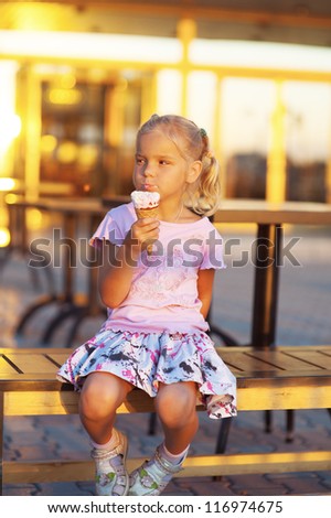 Beautiful little girl sitting on bench and eating delicious ice cream.