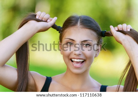 Beautiful dark-haired funny young woman holds up their tails, against background of summer green park.