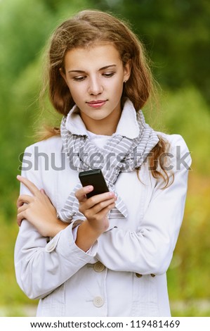 Young beautiful woman reading text message on your mobile phone, against background of autumn park.