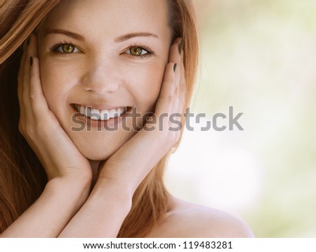 Portrait of smiling beautiful young woman with bare shoulders close up, against green of summer park.