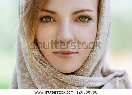 Portrait of calm beautiful young woman in head scarf close up, against green of summer park.