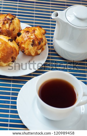 Small muffins on plate, jug of milk and cup of tea on blue bamboo table cloth.