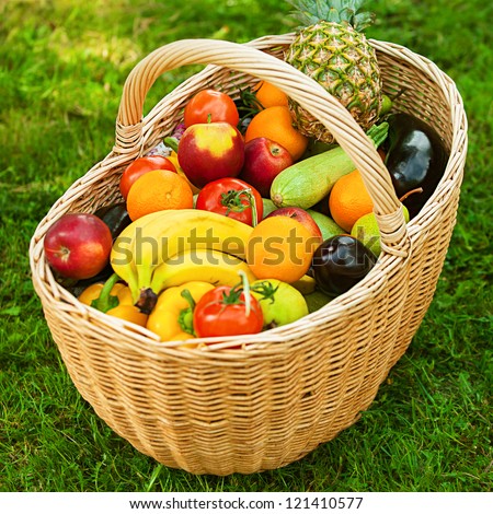 Large wicker basket with fruits and vegetables is on green grass.