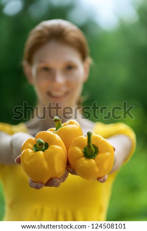 Portrait of red-haired smiling beautiful young woman in yellow blouse with bell pepper, against green of summer park.