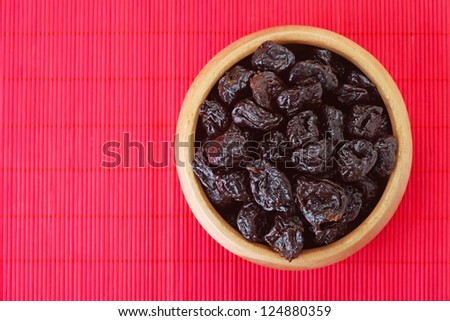 Dried prunes in wooden bowl on red bamboo table cloth.