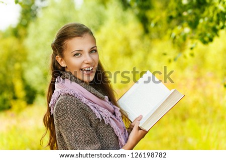 Young funny beautiful woman reading book, against background of autumn park.