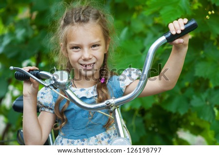 Portrait of beautiful smiling little girl with children\'s bicycle, against background of summer city park.