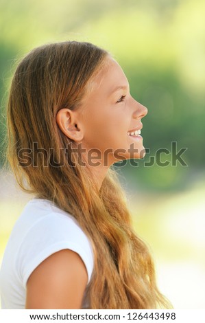 Portrait of young beautiful smiling girl in profile, against green summer garden.