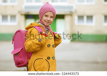 Beautiful smiling little girl in yellow coat with pink backpack goes to school.