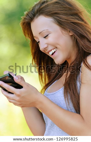 Beautiful smiling young woman writing with stylus on device, against background of summer green park.